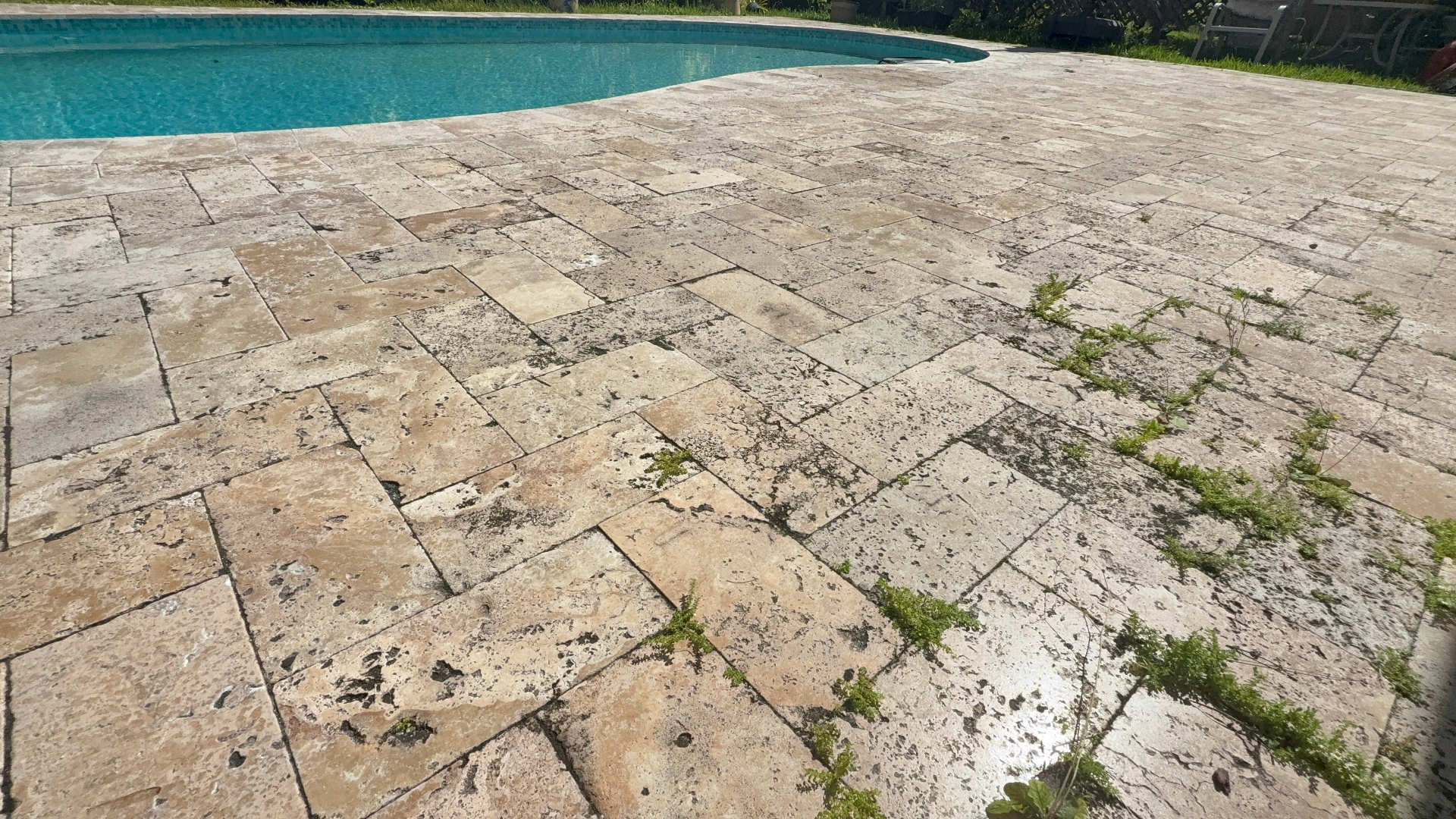 Weathered travertine pool deck with weeds and staining before restoration