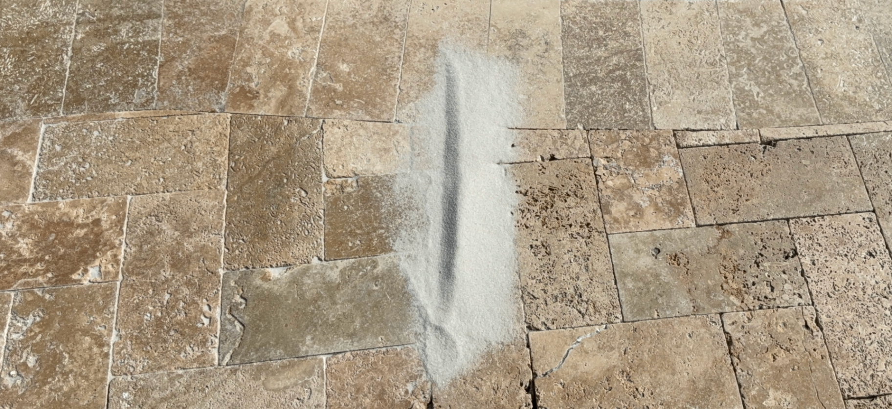 Fresh polymeric sand being swept into travertine joints — before and after in one shot
